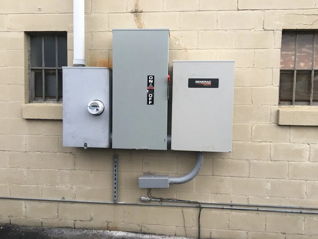 Meter, disconnect and Generac transfer switch mounted side by side on a block wall