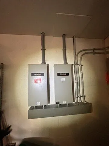 Two Generac transfer switches mounted side by side indoors with conduit above