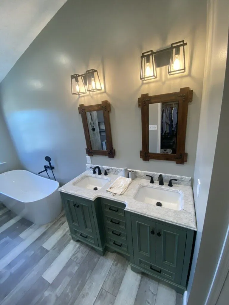 Remodelled bathroom with a green double vanity, two sconces and a freestanding tub