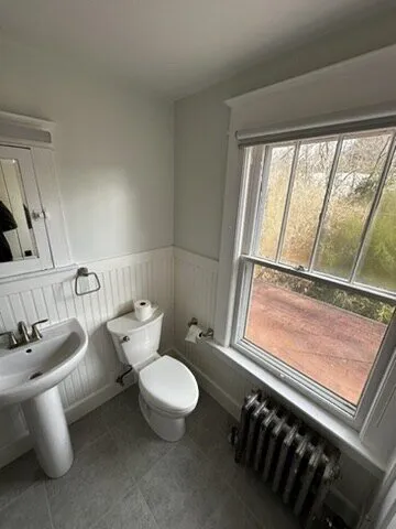 Bathroom with a pedestal sink, toilet and wainscoting by a window