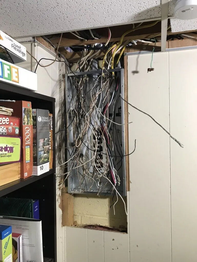 Old panel opening in a wall with tangled wiring exposed, before replacement