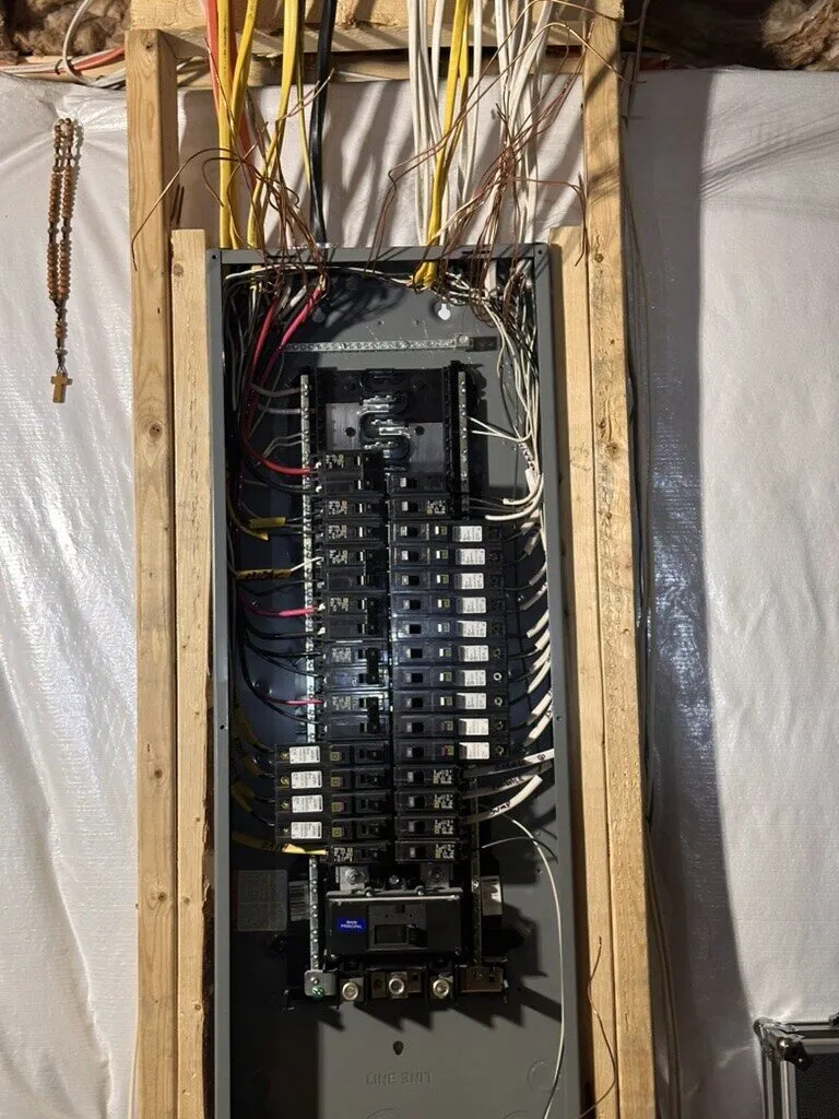 New breaker panel framed into a basement wall with wiring entering from above