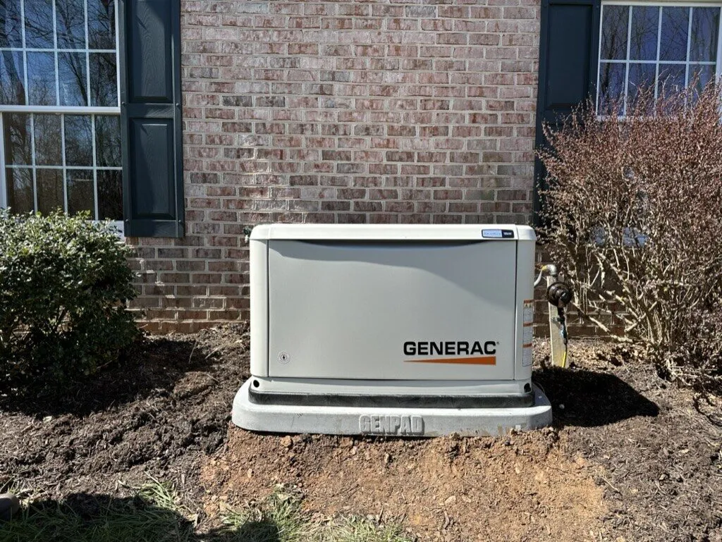 Generac standby generator on its pad in a fresh mulch bed against a brick house