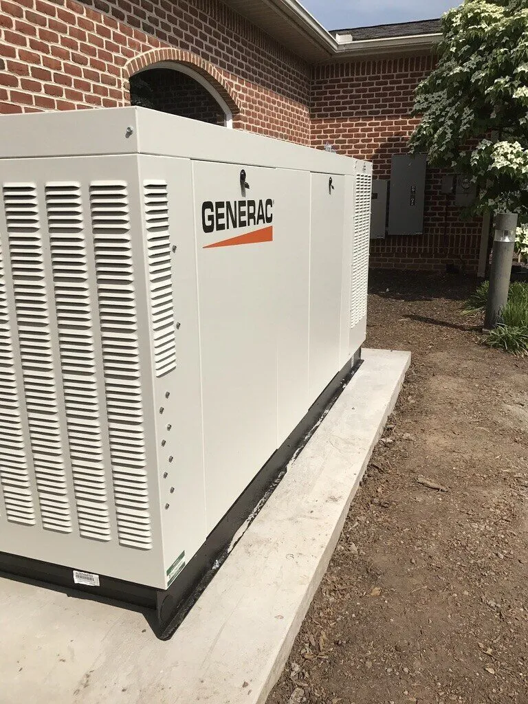 Large Generac generator on a concrete pad along a brick building