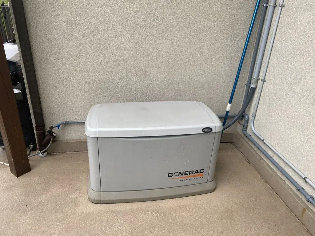 Generac standby generator set in the corner of a concrete patio with conduit along the walls