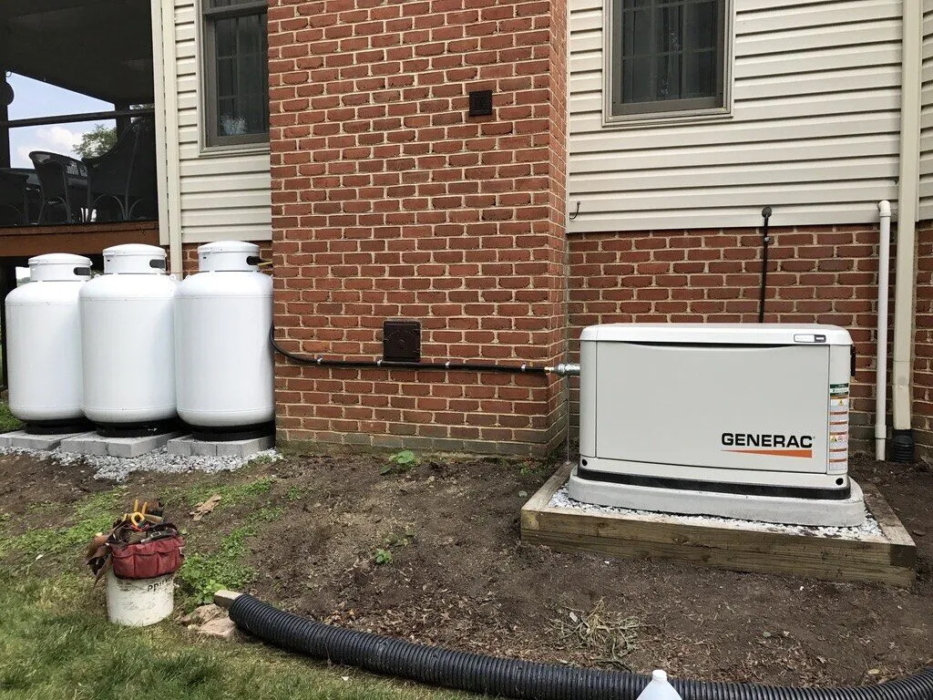 Generac standby generator installed beside a bank of three propane cylinders at a brick and siding home