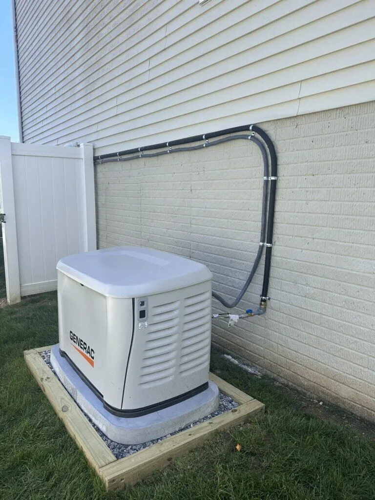 Generac standby generator on a framed gravel pad with conduit routed neatly along the foundation