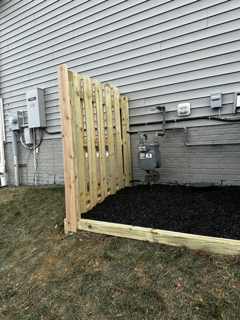 Wood privacy fence screen beside a house with a fresh mulch bed