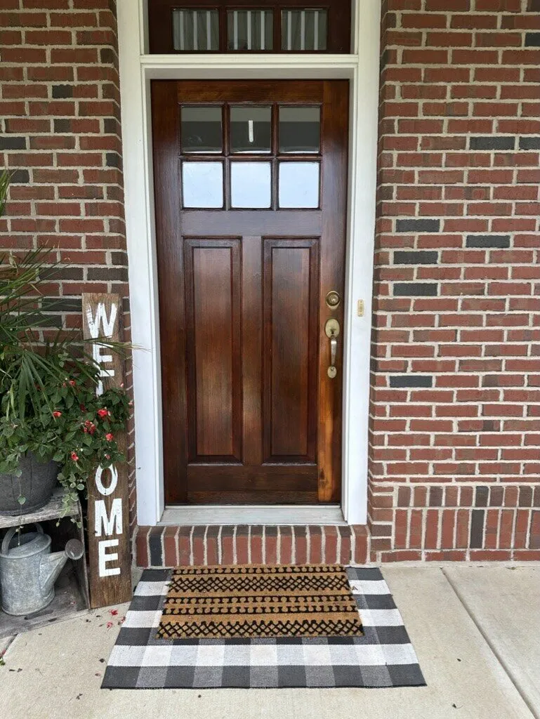 Stained wood front door with a transom window in a brick entry