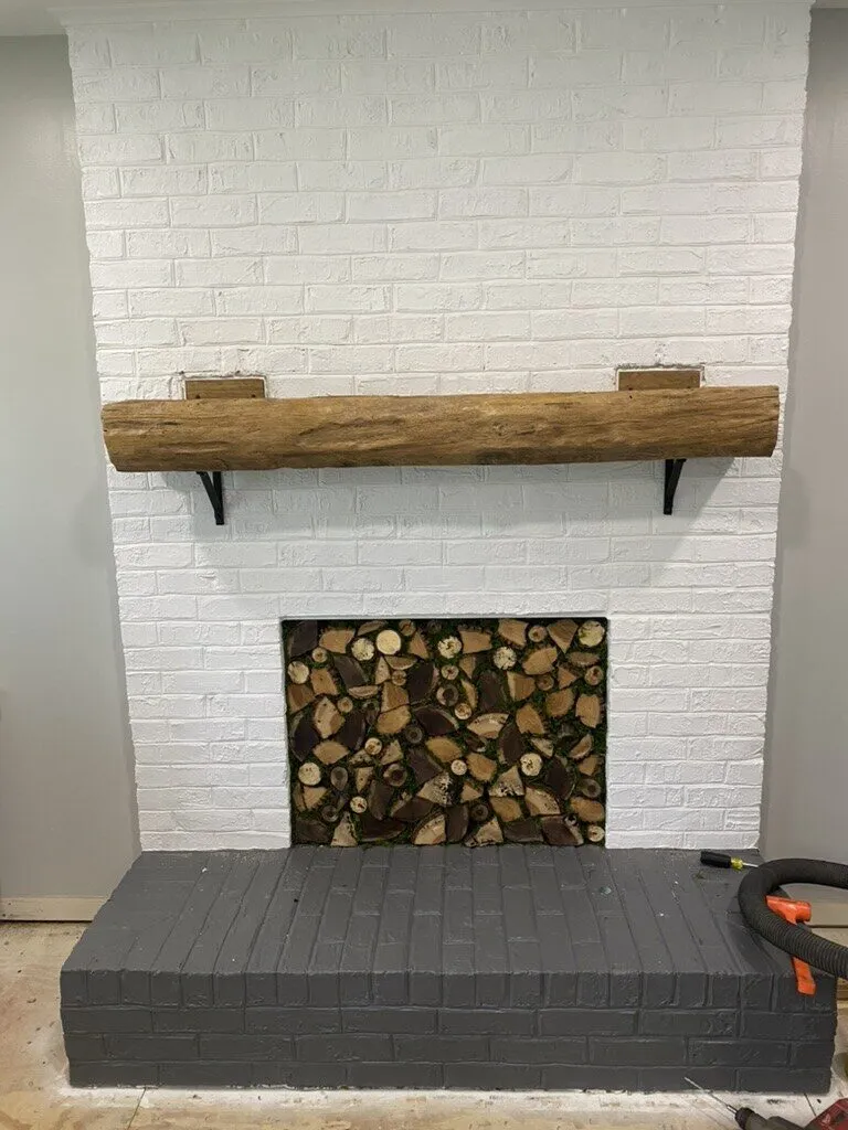 Rough-hewn beam mantel on a white-painted brick fireplace with stacked logs