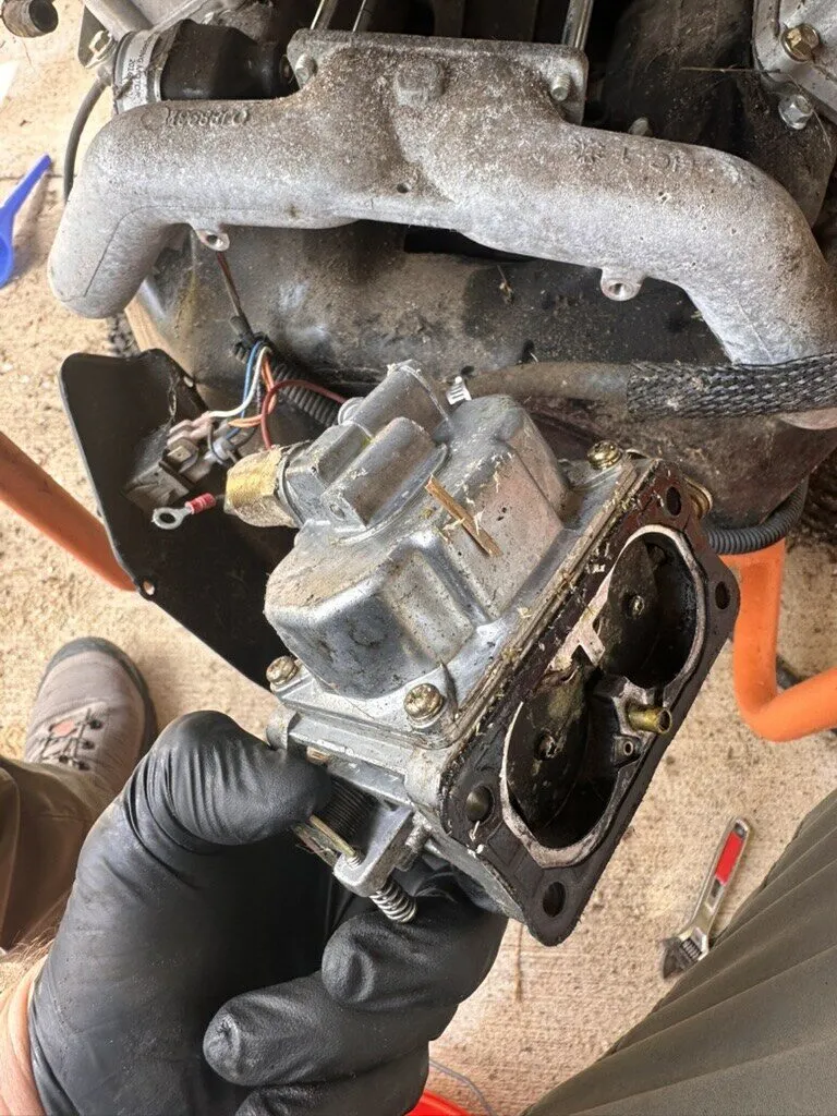 Gloved hands holding a generator carburetor removed from the engine